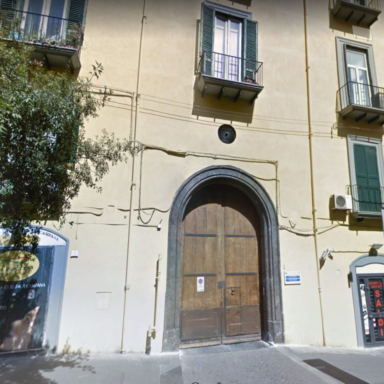 Facciata di un edificio con un grande portone in legno e finestre verdi.
